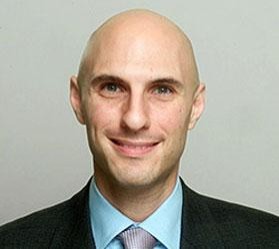 headshot of man wearing black blazer, light-blue collared shirt and light-purple tie