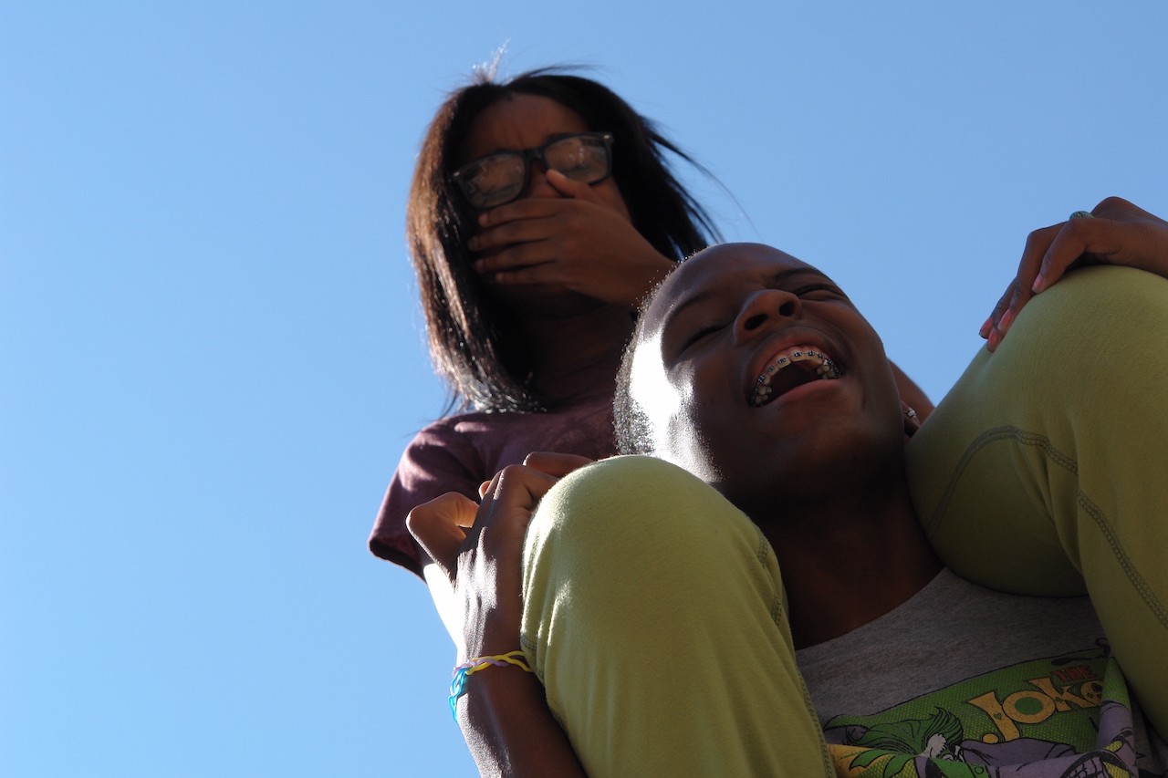 Two teenagers laughing. A young woman is sitting on the shoulders of a young man.