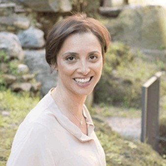 Outdoor headshot of smiling woman with brown hair in an updo