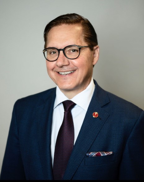 Head and shoulders portrait of a smiling man wearing glasses and a suit and tie.