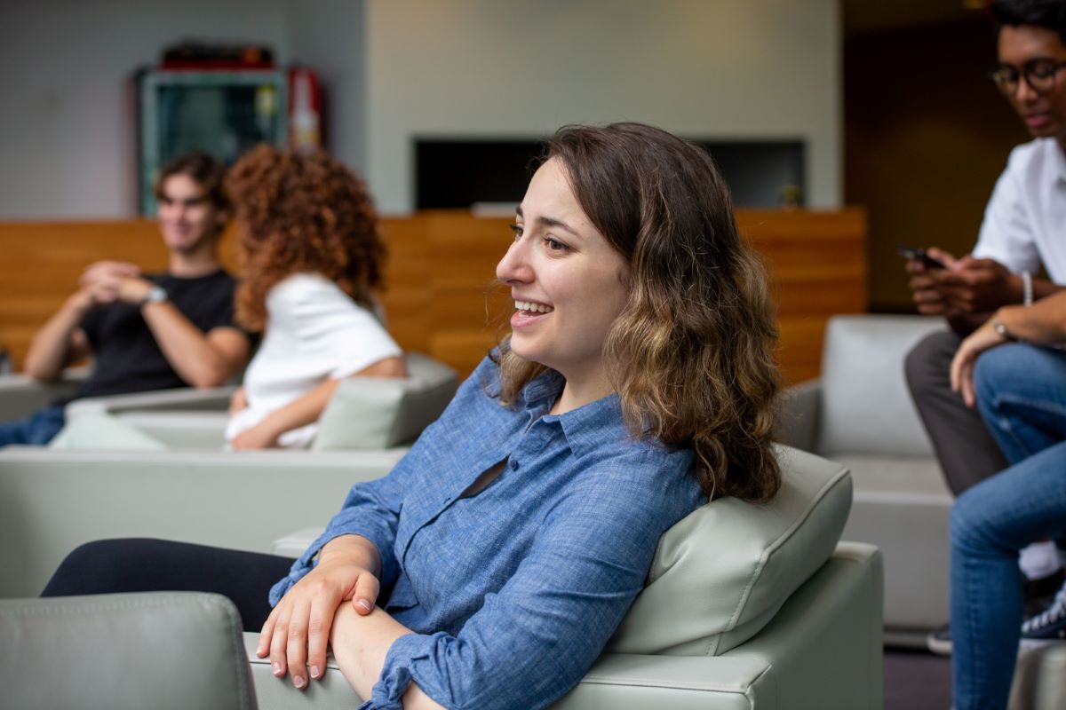 Young woman in the forefront sitting on an armchair, smiling.
