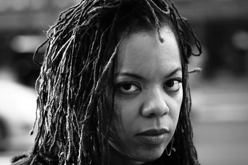 Poet Airea D. Matthews pictured in black and white, her head and face visible, looking directly at camera.