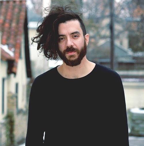 Kaveh Akbar in a black, long-sleeved shirt outside. 