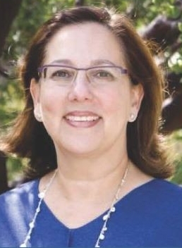 portrait of a woman smiling, wearing blue v-neck shirt, long necklace and glasses