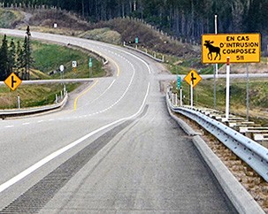 Picture of a fenced highway with an orange and black moose warning sign