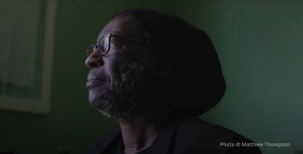 A photo of a man wearing glasses, looking sideways against a dark green background