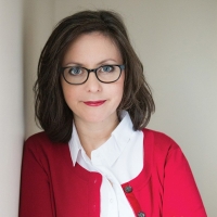 A photo of a brown-haired woman with glasses and a red sweater, taken from teh chest up