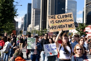 A photo of people outside on a sunny summer day holding signs in a protest demanding climate action