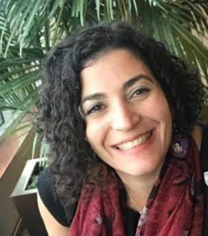A headshot of a smiling brunette wearing a dark red scarf