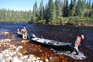 Decorative photo of two men pulling a small fishing boat out of a Canadian river with conifer trees lining the shores