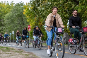 Smiling people biking along a trail with trees on one side