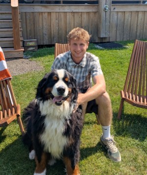 Zachary Yuzda sitting behind a large Bernese Mountain Dog