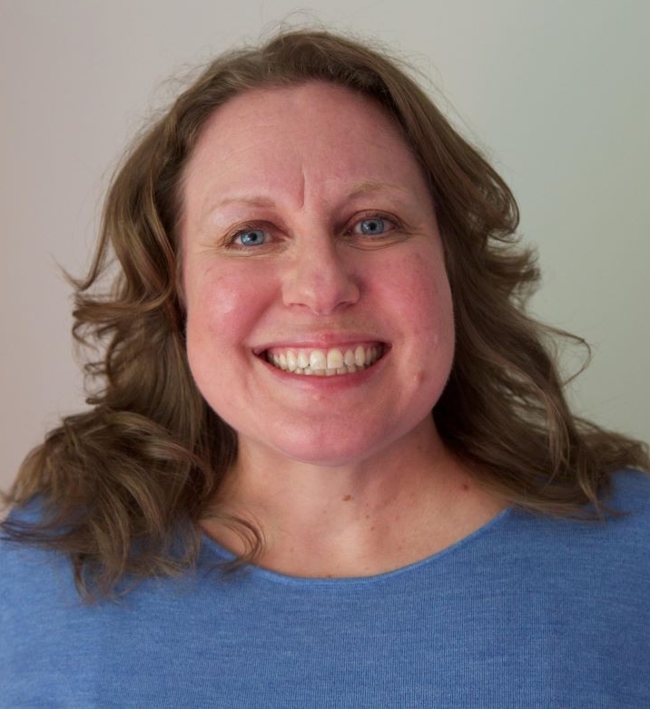 Portrait of blue-eyed smiling woman with shoulder-length hair wearing a blue sweater.