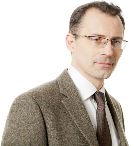 Headshot of brown-haired man with glasses in a grey blazer.