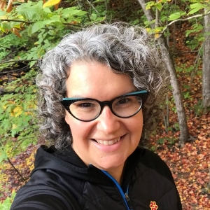 Selfie of Danielle White outside with autumn leaves and evergreen tree in background