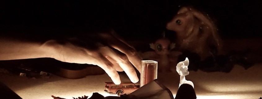 Image depicts a hand under low light. The hand appears to place small objects on a table. 