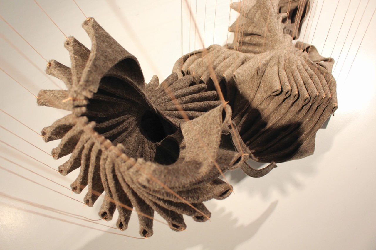 Mylene Raiche's installation shot 318 days displays a piece of felt scraps that are hand-sewn in a particular manner creating a twisted form with structural folds. The abstract shape is suspended with salmon pink nylon treads