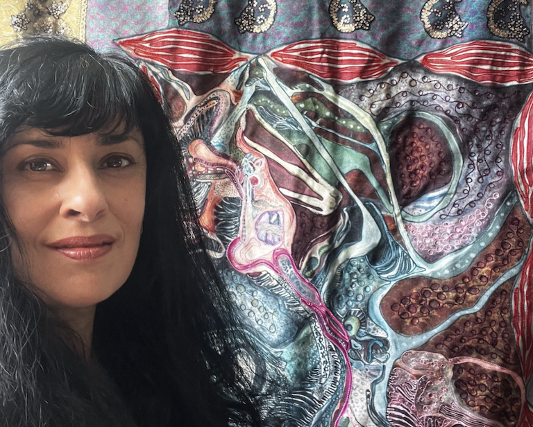 Asma Khan is sitting to the left of a large sewn artwork