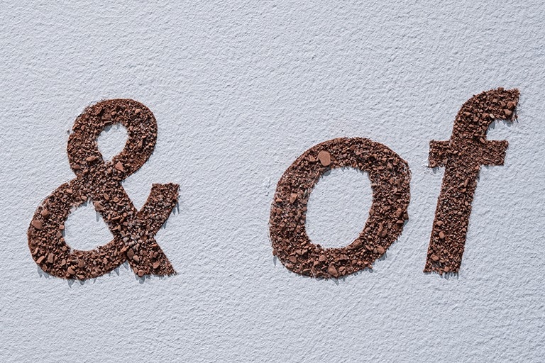 Lettering on a wall made with crushed rocks, characters displayed are "&" and "of"