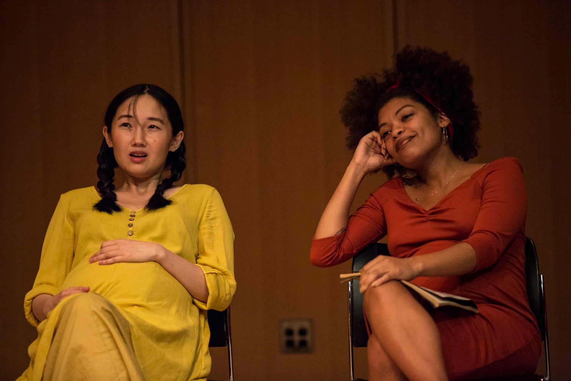 View of two pregnant performers of The Cycles. Both are sitting on chairs and looking in front of themselves.