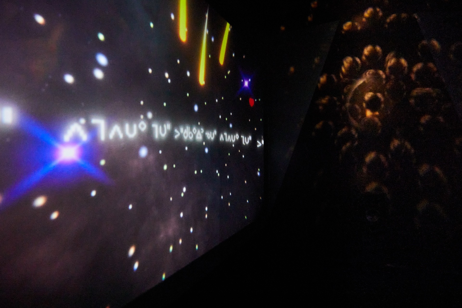Photobgraph of a black room showing a projection of outer space, writing and fragmented light from a sun catcher.