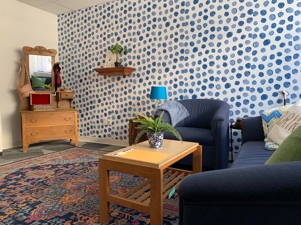 A living room with a blue wallpaper, blue couch and wooden furniture.