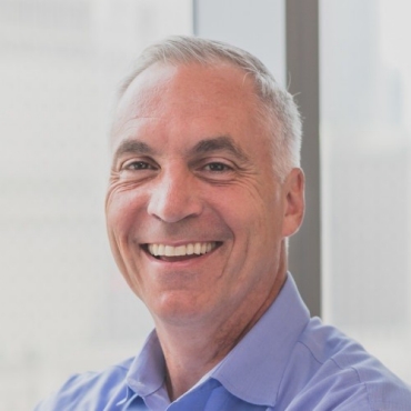 Headshot of smiling man wearing blue shirt in front of blurry window backdrop