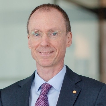 Headshot of smiling man wearing blazer, blue shirt and patterned purple tie