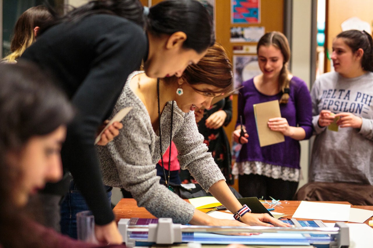 A Sustainability Ambassador is surrounded by students. Everyone is looking down at what is on the table, which is not clear by the camera angle.