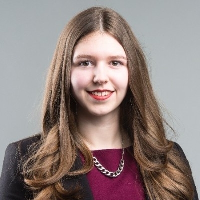 Smiling woman with long brown hair wearing a burgundy top and black blazer