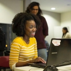 Woman in yellow-and-white shirt smiling at laptop