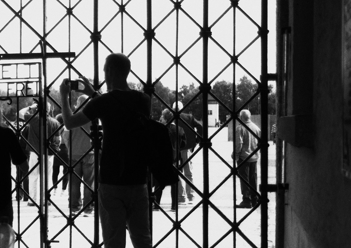 Black-and-white image of the back of a man taking a photo from behind a gate