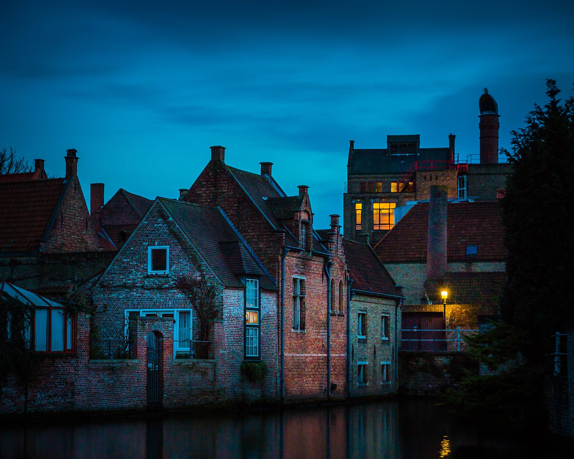 Brick homes at dusk with lights on in the windows and one street lamp illuminated.