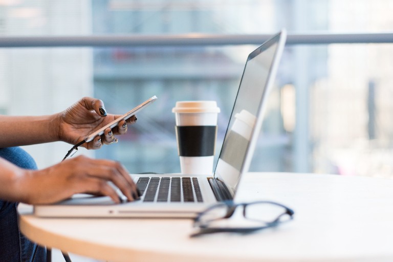 Woman's right hand on laptop and left on cell phone