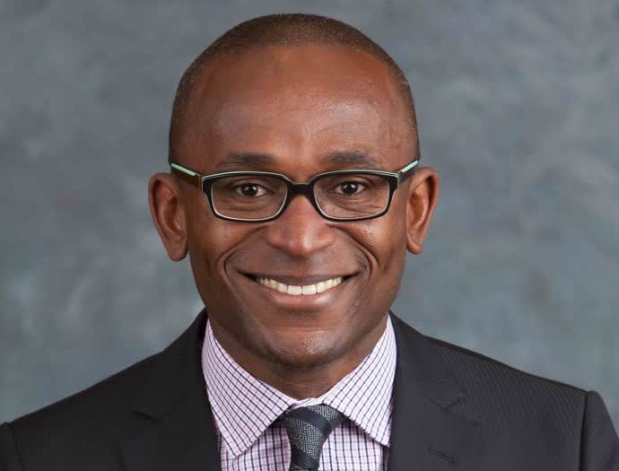 Headshot of smiling man wearing glasses, blazer, collared shirt and tie.