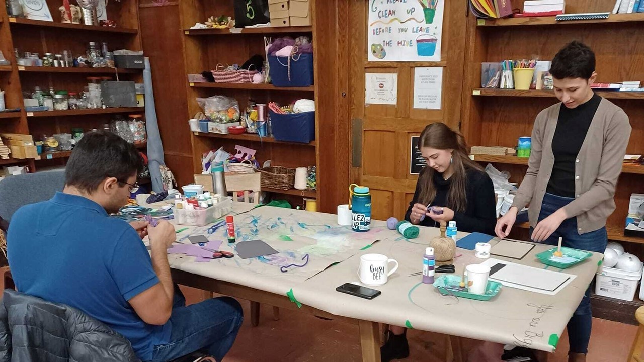 three people sitting and standing around a table, engaged in crafting.