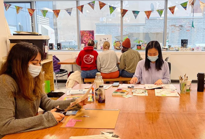 two women sitting at a large table, engaged in crafts.