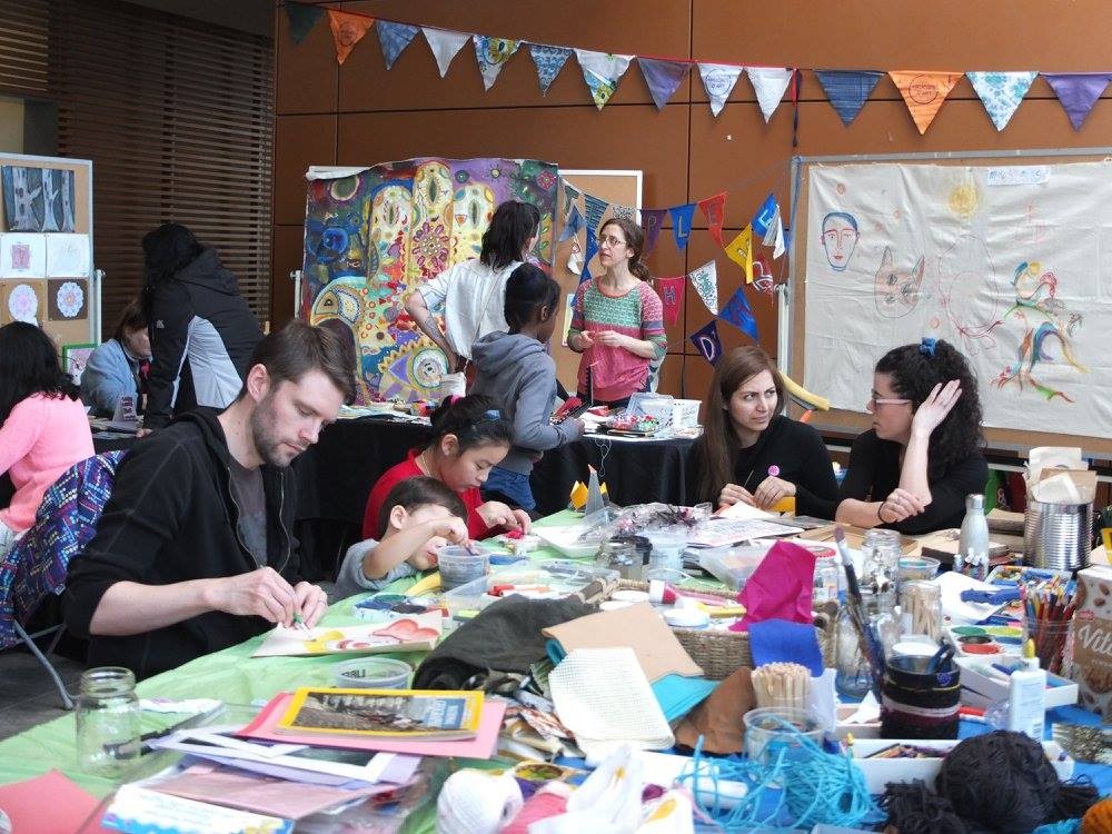 People sitting around a table covered in objects and papers, engaged in crafting.