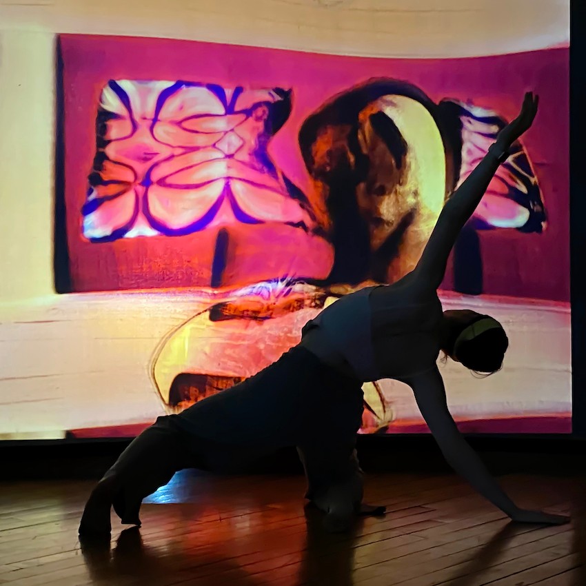 A backlit dancer in a side bend in front of a pink and purple digital projection.