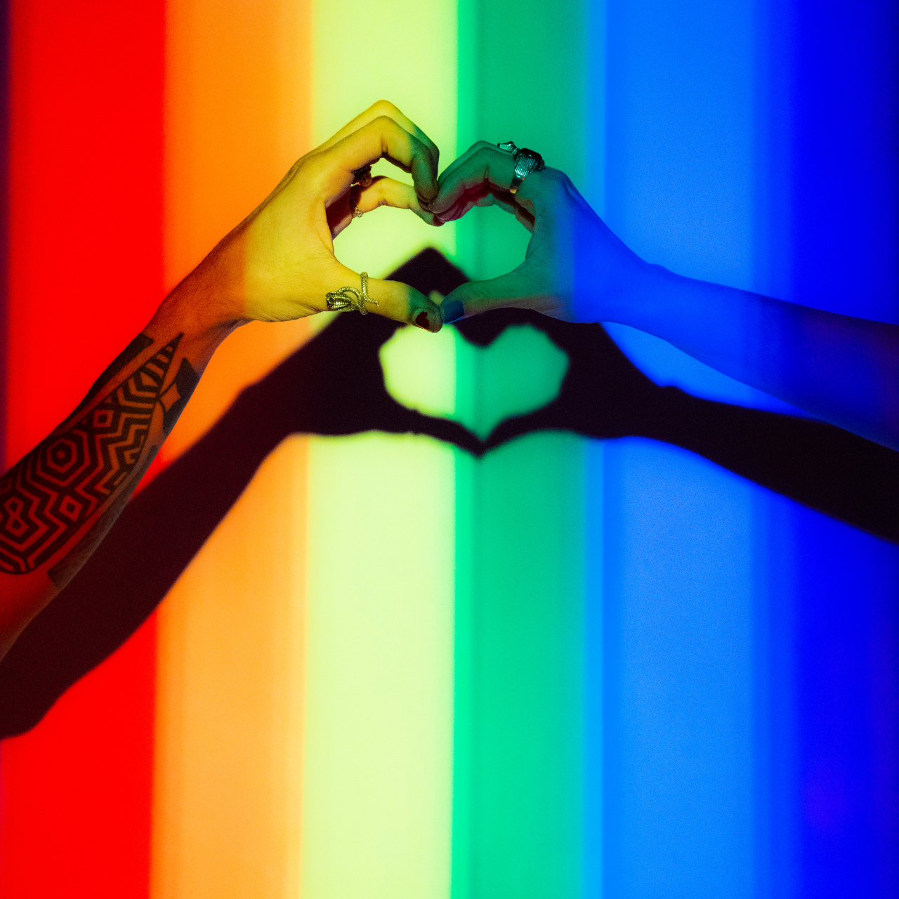Two hands forming a heart against a rainbow backdrop