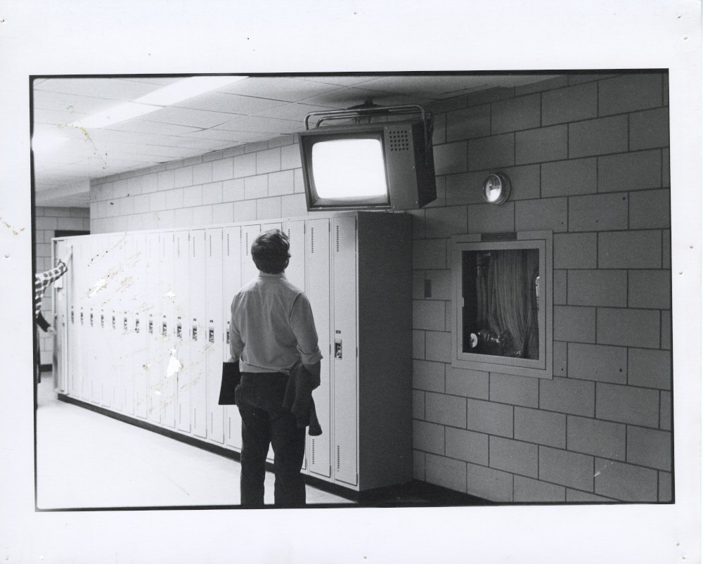 Archival image of an unknown induvidual watching a CUTV monitor in the Hall Building.