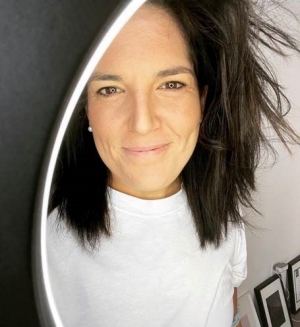 A woman with dark curly hair smiles at the viewer