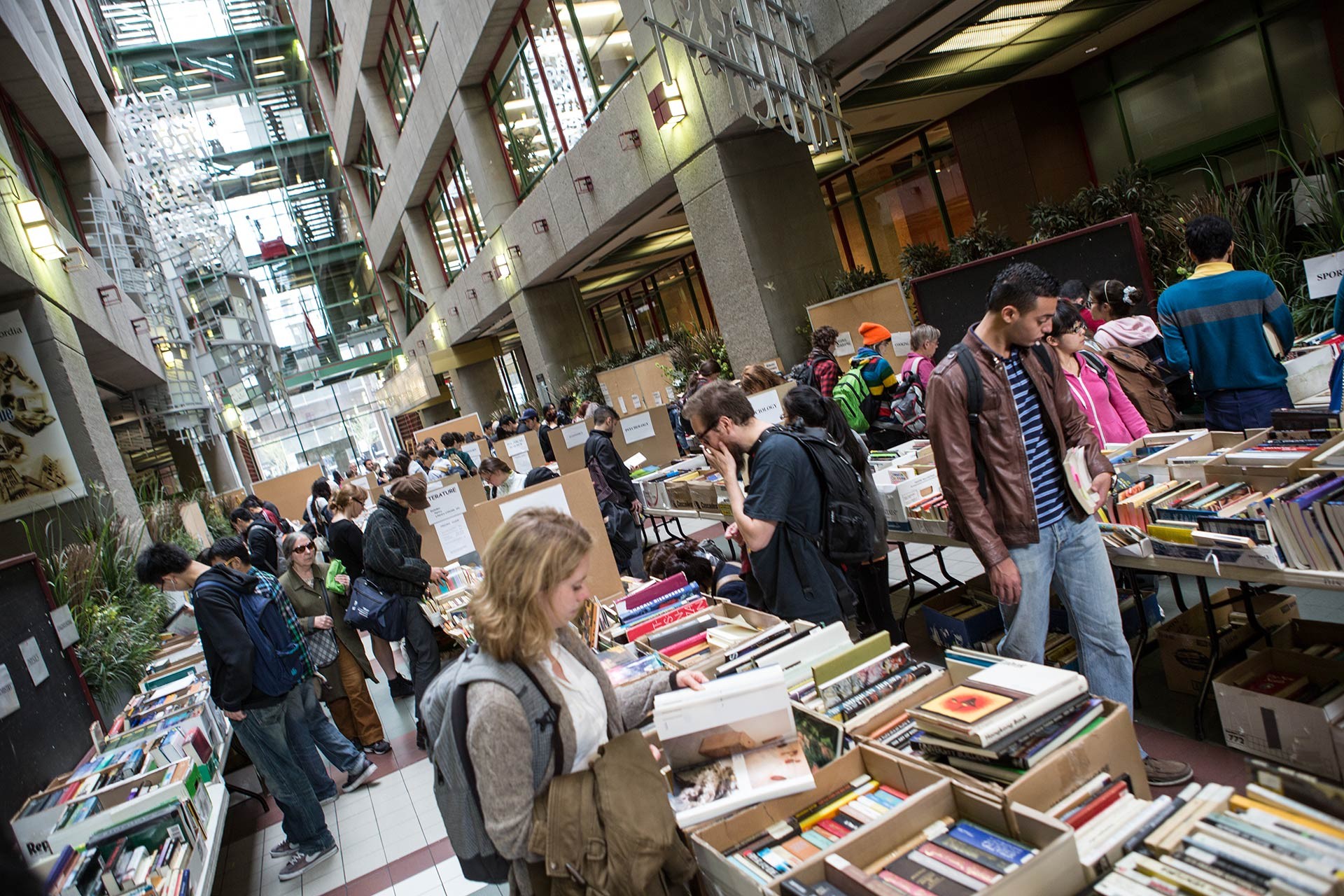 A crowd of people look at and select books from tables set up in an atrium