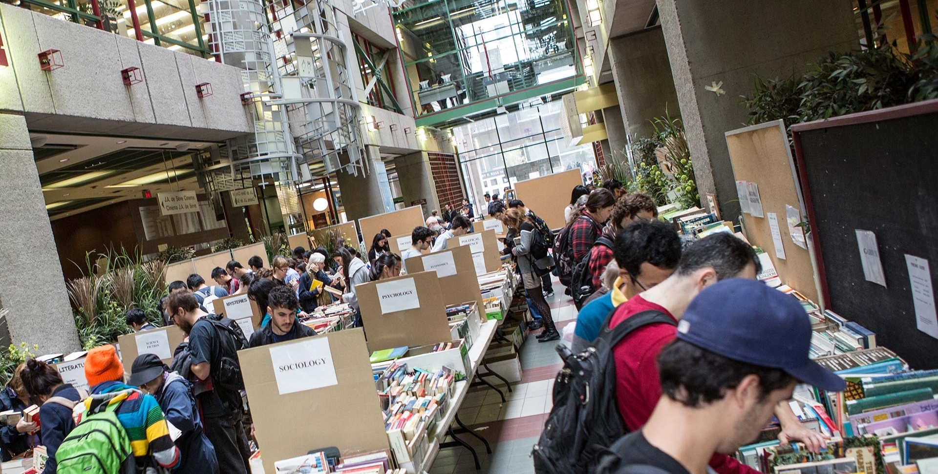 A crowd of people look at and select books from tables set up in an atrium