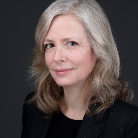 A woman with medium-length grey hair wears black clothing