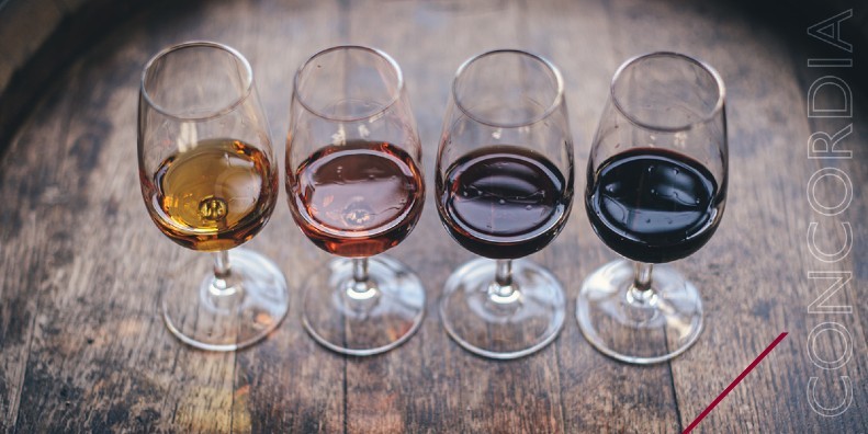 Four glasses of wine are lined up in a row on a wooden table