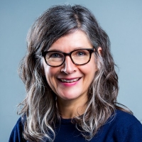A woman with glasses and greying hair wears a navy blue sweater