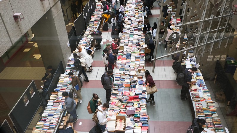 A crowd of people look at and select books from tables set up in an atrium