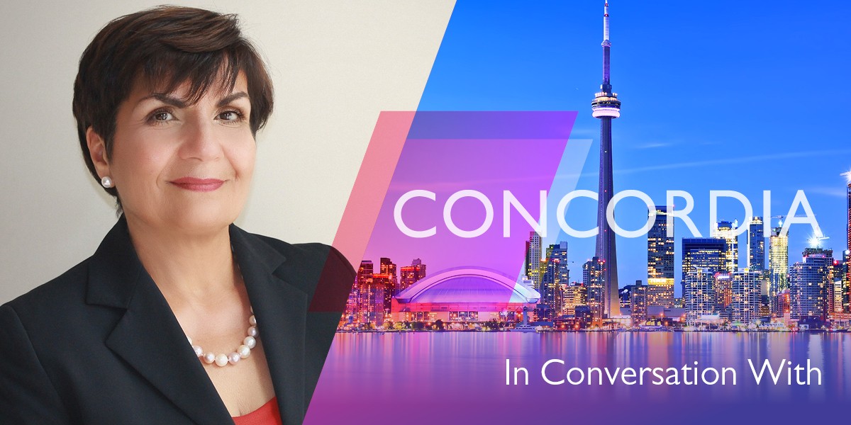 Gina Cody has short dark hair and wears a dark suit jacket against a white background. Her portrait is next to a cityscape.