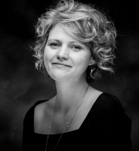 Portrait of woman with curly, light-coloured hair, wearing a black sweater 